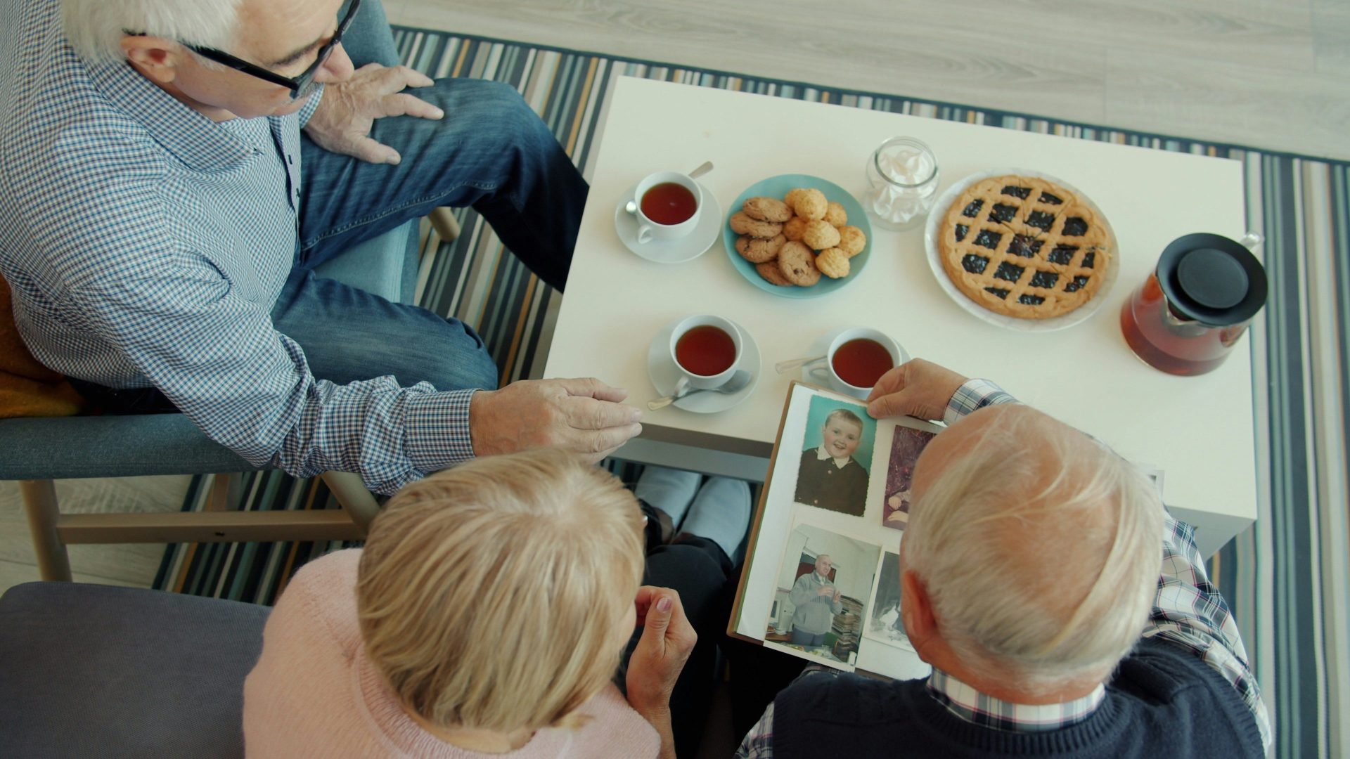 Seniors looking at a photo album with tea and snacks.