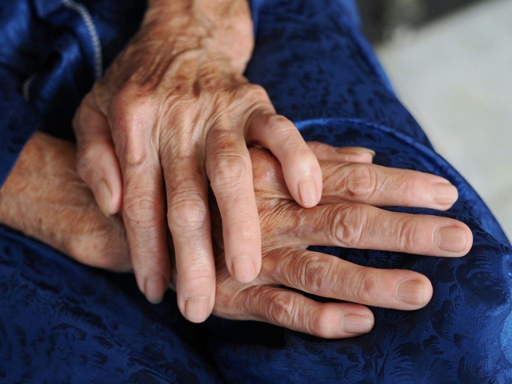 Close-up of elderly hands resting on a blue fabric.